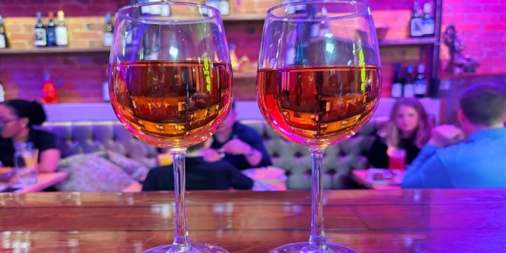 Two wine glasses with pink Bollywood cocktail on a wooden bar.