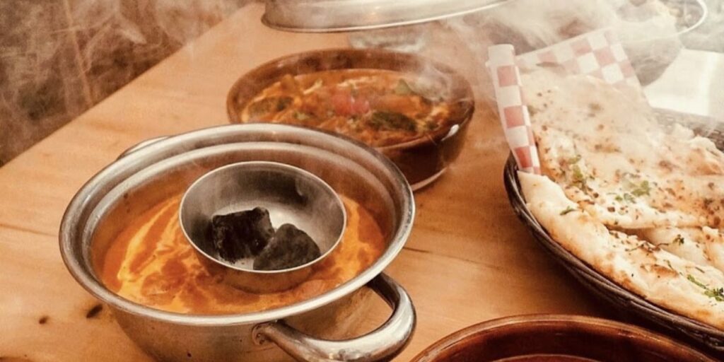 A table with Butter Chicken, a creamy tomato-based curry with tender chicken pieces, and a pot of soup.