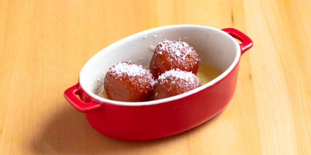 A red bowl filled with sugar-covered doughnuts, reminiscent of Gulab Jamun, a North Indian dessert with deep-fried milk-based balls in sugar syrup.