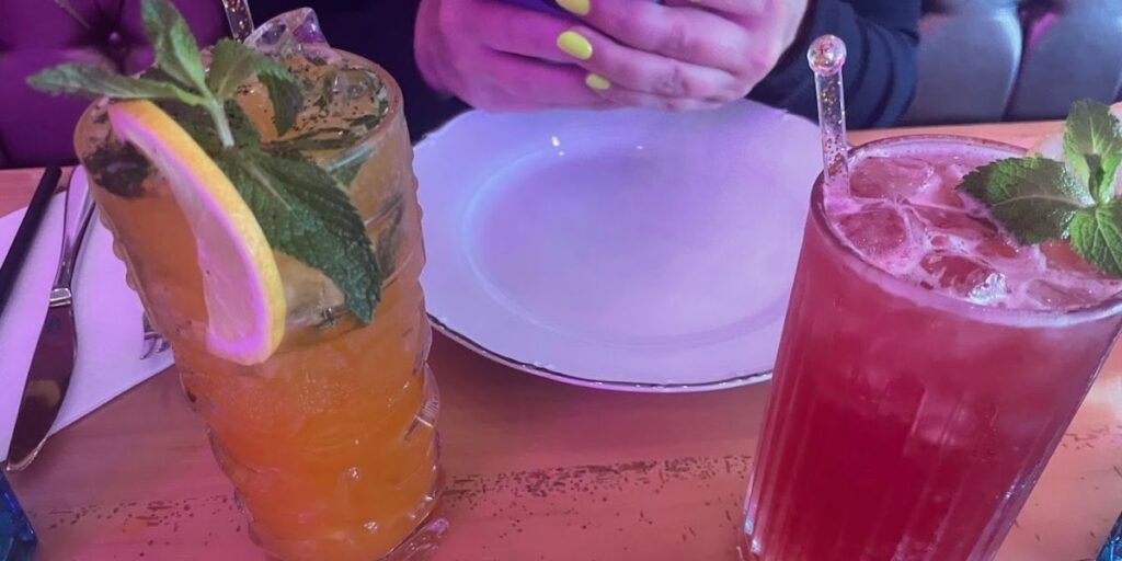 A person holding a cell phone next to two drinks on a table, one of which is a refreshing Minty Mojito cocktail.