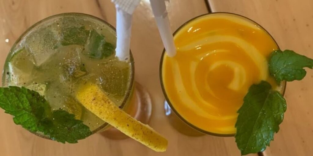 Two Old Fashioned cocktails with ice and mint leaves on a wooden table - a timeless classic at Leela Indian Food Bar.