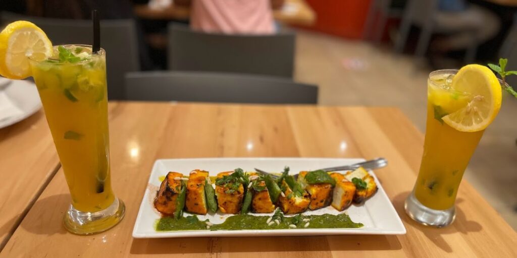 A plate with Paneer Tikka, grilled Indian cottage cheese cubes marinated in spices and yogurt, served with mint chutney and drinks.