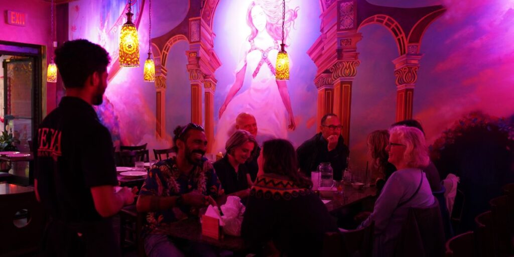 Diners enjoying meals at tables in a restaurant illuminated by purple lights.