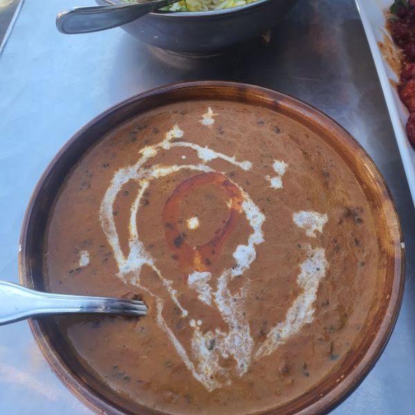 A bowl of rich Dal Makhani soup with a spoon resting beside it, showcasing expert Indian culinary craftsmanship.