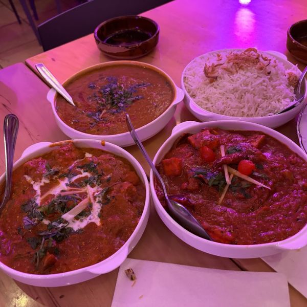 A table set with four bowls of exquisite Indian food, emphasizing the vibrant colors and artistic presentation of the culinary creations.