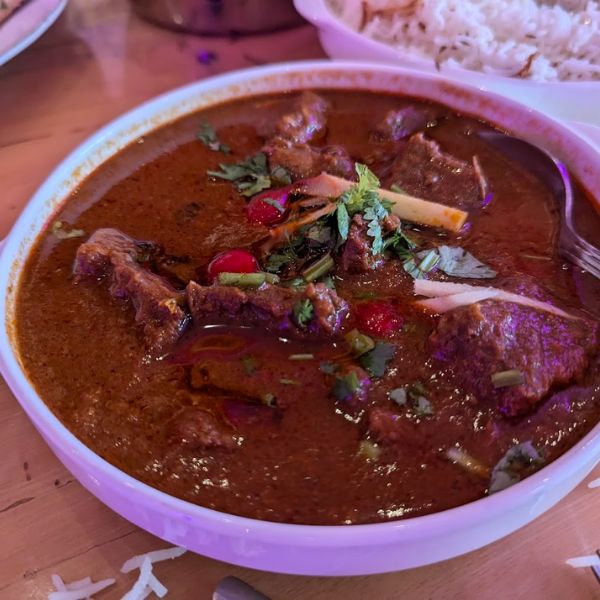 A bowl of Chicken Kadhai curry on a table, accompanied by rice and various dishes, symbolizing cultural connection and community.